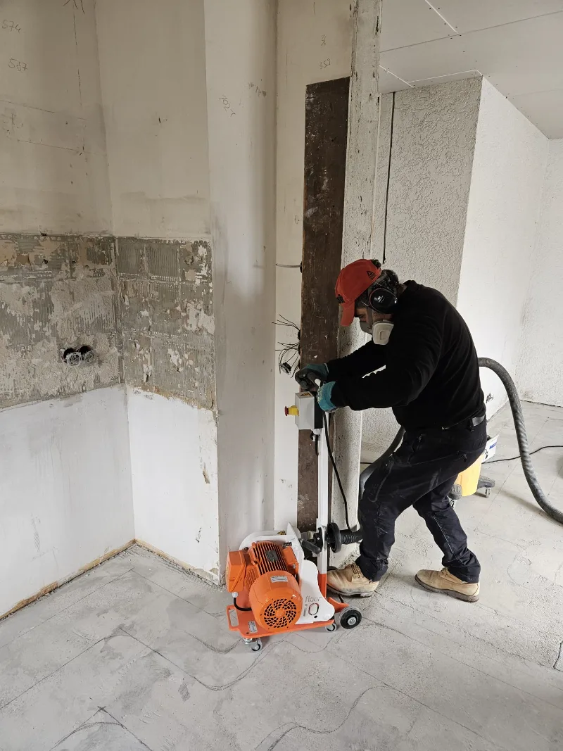 Gefräste Kanäle laufen bis an Wand und Raumecke; die Fräse steht auf dem freigelegten Estrich.
